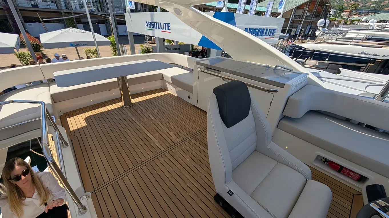A spacious luxury yacht deck featuring wooden flooring, a comfortable seat, and an elegant white seating area in bright sunlight.